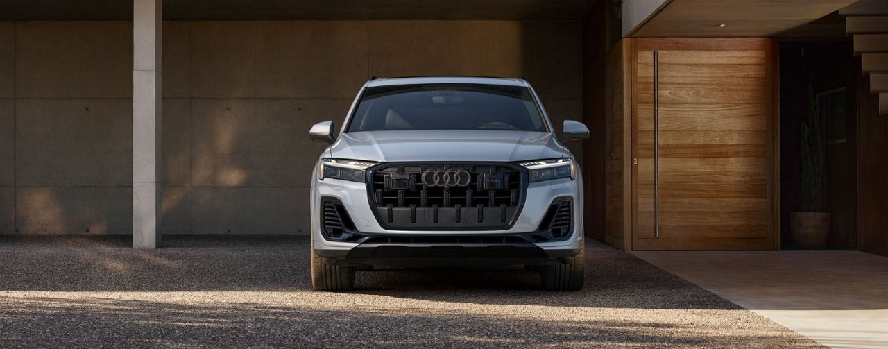 A silver 2025 Audi Q7 parked in front of a home garage door.